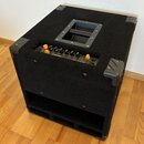 Černý basový kombozesilovač s povrchem z textilie a plastovými ochranami rohů. Na horním ovládacím panelu jsou žluté a černé ovratové knofíky a nápis…