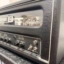 Detail kytarového komba v černém koženěném potahu. Na horním pro suốtu je bílý nápis TUBE AMP DESIGN BY Bogner a část jiného nečitelného loga. Přední…