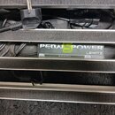 Fotografie zachycuje napájecí zdroj pro efektové pedály umístěný v rackovém systému s černými kabely. Na šedém předním panelu je bílý nápis PEDAL POW…