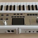 Bílá klávesová syntezátor s nápisy KORG a microKORG. Přístroj má ovládací panel s řadou tlačítek, knoflíků a malým displejem uprostřed. Na spodní hra…