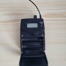 Černý bezdrátový přijímač z plastu s vyklopeným krytem baterií a anténou. Na přední straně je malý displej, tři kontrolky s nápisy LOW BATT, ON a RF,…