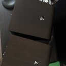 Dva tmavě hnědé dřevěné reproduktory s hranatým tvarem. Na přední straně každého z nich je umístěn malý kulatý černý štítek s bílým logem ve tvaru st…