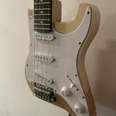 Elektrická kytara s přírodním dřevěným povrchem těla a bílým pickguardem. Nástroj má tři bílé snímače typu single-coil, jeden bílý přepínač a dva bíl…