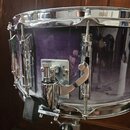 Fialový snare drum s chromovaným obručováním a mechanismem. Na korpusu jsou vidět stopy opotřebení v podobě drobných škrábanců a znečištění povrchu.…