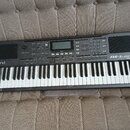 Černý digitální klavír s bílými a černými klávesami. Na levé straně je bílý nápis Roland a vpravo nápis EXR-5s INTERACTIVE ARRANGER. Horní panel obsa…