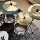Celá bicí souprava s několika činely a bubny. Na činelech je vidět logo a nápis Istanbul Agop a označení Xist. Bubny mají na blanách nápisy EVANS a T…