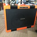 Kytarový kombozesilovač v oranžovém provedení s černými pruhy. Na horní části je nápis Fender-Deluxe a uprostřed mřížky značka HRDX. Povrch je lesklý…
