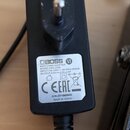 Černý síťový adaptér s viditelným kolíkem konektoru. Na bílém štítku je uvedeno logo BOSS, nápis SWITCHING ADAPTER a MODEL:PSA-230S. Jsou zde uvedeny…