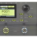 Šedý kytarový procesor s černým displejem a expresním pedálem. V levém horním rohu je nápis GE200 a pod ním menší text MULTI-EFFECTS GUITAR PROCESSOR…
