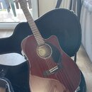 Akustická kytara s cutawayem v tmavě hnědé barvě, umístěná v černém tvrdém pouzdře. Na hmatníku je viditelné logo Fender a nápis BASIC SERIES. Povrch…