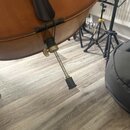 Detailní pohled na spodní část smyčcového nástroje z hnědého dřeva. Je zde vidět kovový endpin s černou gumovou patkou a šroubovacím mechanismem pro…