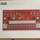 Fotografie znázorňuje krabici s červeným analogovým bicím automatem. Na krabici je nápis RD-6-SB Analog Drum Machine with 8 Drum Sounds, 64 Step Sequ…