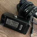 Černý napájecí adaptér s kabelledmi a konektorem. Na spodní části je nápis tc electronic, DESIGNED AND ENGINEERED a text s technickými parametry včet…