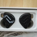 Dva černá vaušní sluchátka s ergonomickým tvarem umístěná v bílém plastovém pouzdře. Na horní části obou sluchátek je nápis 10 HYBRID TECHNOLOGY. Na…