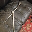 Na fotografii je kovový, chromovaný stojan nebo držák s teleskopickým mechanismem. Horní část končí černým plastovým knoflíkem. Povrch kovu vykazuje…