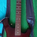 Elektrická kytara s trupem v barevnosti sunburst a hnedým krčkem, umístěná v otevřeném kufru s zeleným vnitřkem. Nástroj má jeden humbucker snímač, t…