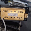Fotografie zachycuje zadní stranu elektrického snímače v černém plastovém rámečku. Snímač má mosazný kryt s viditelným oxidovaním a povrchovými nečis…