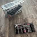 Na fotografii je kytarový efektový procesor Boss ME-80 v šedé barvě s černým pedálem výrazu. Za přístrojem je umístěna originální krabice s nápisy BO…