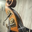 Detail hlavy smyčcového nástroje, pravděpodobně kontrabasu, vyrobené z dřeva s hnědým lakem. Na viditelné straně jsou dva kovové ladičky s ozubenými…