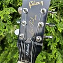 Fotografie zachycuje hlavu černé elektrické kytary s nápisy ve zlaté barvě. V horní části je logo Gibson, uprostřed nápis Les Paul MODEL a v dolní čá…