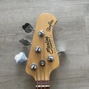 Fotografie zachycuje hlavu basové kytary z přírodního světlého dřeva s chromovanými ladičkami. Na hlavě je černý nápis Sterling by MUSIC MAN a StingR…