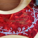 Detail červeného plechtru s mramorovým vzorem na světlém dřevěném povrchu nástroje. Na plechtru je umístěna bílá ornamentální dekorace v podobě větví…