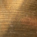 Detailní záběr na povrch mosazného činelu. Je na něm vyryto logo SABIAN, pod ním jsou soustředné půlkruhy a v dolní části nápis CANADA. Povrch vykazu…