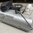 Stříbrný kouřový stroj z kovu s bílou plastovou nádržou na tekutinu. Na přístroji jsou nápisy „Antari“, „Z-1200 SMOKE FOGGER“ a „Z 1200 series“. Povr…