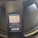 Detailní záběr na zadní část černého reproduktoru. Na rámu je nalepený modrý štítek s bílým textem: RCF PRECISION, M1810-SW1801 LOW FREQUENCY TRANSDU…