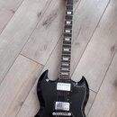Černá elektrická kytara s dvojsekyrou v tvaru SG. Na hlavě hmatníku je bílý nápis Urville a zlatý znak. Nástroj má dva humbuckery, stříbrný most s ko…