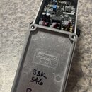 Fotografie znázorňuje otevřený efekt pedál v hliníkovém šedém šasi. Uvnitř je viditelná elektronická deska s komponenty a zapojením kabelů. Na vnitřn…