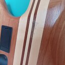 Detailní záběr na tělo elektrické kytary z dřeva s výraznou masivním žilováním. Uprostřed jsou dva paralelní tmavě hnědé pruhy dřeva zasazené do svět…