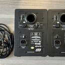 Dva černé studiové monitory z pohledu zadní strany a svazek černých napájecích a signálních kabelů. Na každém reproduktoru je bílý nápis aktiv 05, lo…