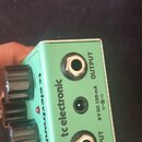 Zelený efekt pedál značky tc electronic. Na horní hraně jsou konektory s nápisy OUTPUT a INPUT a vstup pro napájení s označením 9 V DC 100 mA. Na bok…