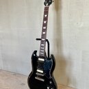 Černá elektrická kytara s dvojsečným tělem umístěná na černém stojanu. Na hlavě hmatníku je viditelné logo Epiphone. Nástroj má dva humbuckery, stříb…