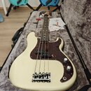 Bílá elektrická basová kytara v černém polotvrdém kufru s šedým polstrováním. Nástroj má hnědý želvový pickguard a chromovaný most. Na hlavě krku je…