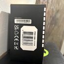 Fotografie zachycuje černou papírovou krabici s bílými nápisy a štítky. Na krabici je uveden text SERIAL NUMBER a pod ním kód (21)152.610/19538/0173.…