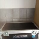 Černý transportní case s hliníkovými hranami a kovovými vršky. Na přední straně je bílý nápis MESA/BOOGIE a pod ním text The Spirit of Art in Technol…