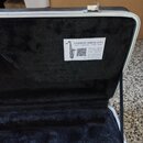Otevřený kufřík s černým plyšovým vnitřkem. Na vnitřní straně víka je nalepený bílý štítek s nápisem SAXOFON SERVIS JAŠA, Opravy, nákup a prodej hude…