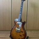 Elektrická kytara s prohnutou deskou z plaménového dřeva v hnědém sunburst provedení. Na hmatníku jsou vyznačeny vložky ve tvaru ptáků a na hlavě je…