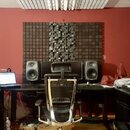 Fotografie zachycuje domácí hudební studio s černým pracovním stolem a ergonomickou židlí. Na stole jsou umístěny dva šedé studiové monitory, noteboo…