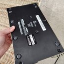 Fotografie zachycuje spodní stranu černého elektronického zařízení s několika gumovými nožičkami a šrouby. Na spodní části jsou umístěny bílé textové…