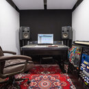 Fotografie zachycuje hudební studio s pracovním stolem, na kterém je umístěna míchací konzole a monitor počítače. Na stole jsou dva studiové monitory…