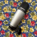 Stříbrný kondenzátorový mikrofon s černou mřížkou a černým držákem. Na horní části je bílý nápis SAMSON a pod ním menší text C01 STUDIO CONDENSER. Po…