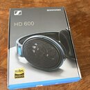 Fotografie znázorňuje krabici od sluchátek. Na šedém povrchu krabice je bílé logo Sennheiser, nápis SENNHEISER a modelové označení HD 600. V levém do…