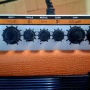 Detail ovládacího panelu oranžového kytarového komba. Na stříbrném panelu je nápis ORANGE CRUSH 20 a řada ovládacích prvků s popisky PHONES, AUX, CHA…