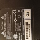 Fotografie zachycuje detail černého štítku s technickými údaji a certifikacemi. Na štítku je uveden SERIAL NUMBER 2034070CWFU0882 a REVISION C03. Jso…