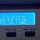 Detailní záběr na modře podsvícený displej elektronického zařízení s kovovým povrchem. Na displeji jsou nápisy CH1, CH2, PRESET a v řadě zkratky Y, X…