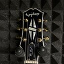 Fotografie zachycuje hlavu černé elektrické kytary s bílým lemováním. V horní části je bílé logo Epiphone a v dolní části nápis Les Paul CUSTOM. Upro…