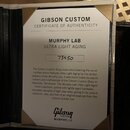 Fotografie znázorňuje certifikát pravosti v černém pouzdře. Na dokumentu jsou texty GIBSON CUSTOM, CERTIFICATE OF AUTHENTICITY, MURPHY LAB a ULTRA LI…